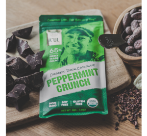 Bar of K'ul Peppermint Crunch Dark Chocolate sitting on a cutting board, surrounded by different forms of chocolate