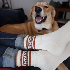 Crossed feet wearing ivory Tony's Vintage Socks with burnt orange cuff and smiling dog in background