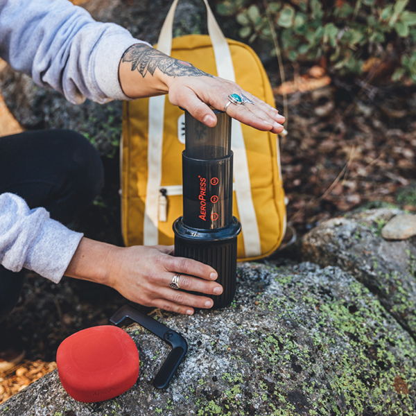 Person outdoors with a yellow backpack using an Aeropress Go