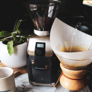 Baratza Virtuoso + Grinder sitting on a marble counter with a plant and a chemex brewer