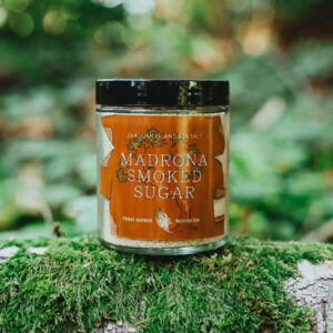 Jar of San Juan Island Sea Salt Smoked Madrona Sugar sitting on top of a mossy log