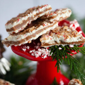 Close up of peppermint bark toffee sitting on a raised red platter with cedar branches